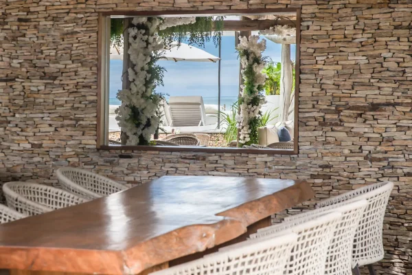 Preabeach restaurant stone wall with mirrored window framed by white flowers, terrace view